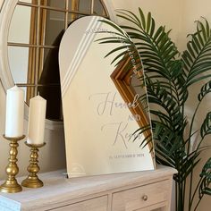 a mirror and some candles on a table with a plant in front of the mirror