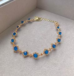 a gold bracelet with blue stones on it in a white box, the bracelet is made out of glass beads