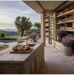 an outdoor kitchen with wooden counter tops next to a swimming pool and olive trees in the distance