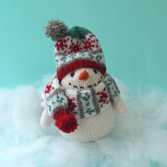 a knitted snowman with a hat and scarf on top of white fluffy clouds