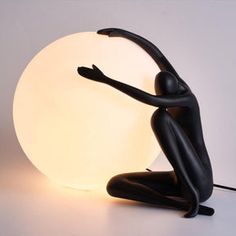 a black figurine sitting on the ground next to a light that is turned on