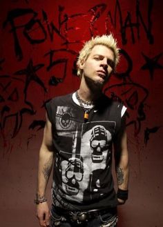 a man with blonde hair standing in front of a wall covered in grafitti