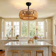 a kitchen island with two stools under a chandelier in front of windows