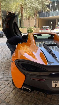 an orange and black sports car parked in front of a tall building with palm trees