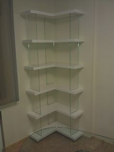 a white shelf with glass shelves in the corner on each side and an empty wall behind it