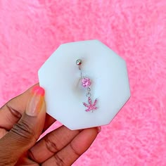 a person holding up a white piece of glass with pink flowers on it and a dangling bead in the middle