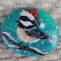 a painted rock with a bird wearing a santa hat on it's head, sitting on a white blanket