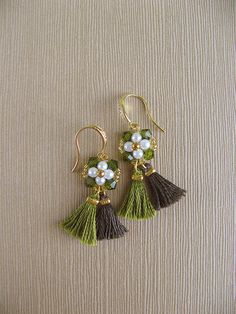 two pairs of earrings with flowers and tassels on them, sitting on a beige surface