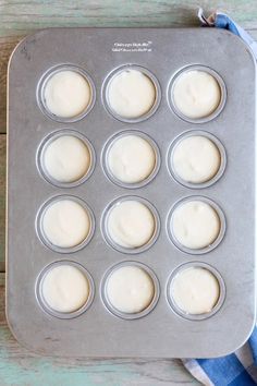 a muffin tin filled with white frosting on top of a wooden table next to a blue napkin