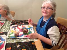 two young children sitting at a table with cupcakes and frosting in front of them