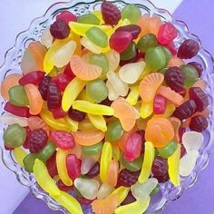 a glass bowl filled with lots of gummy bears on top of a purple table