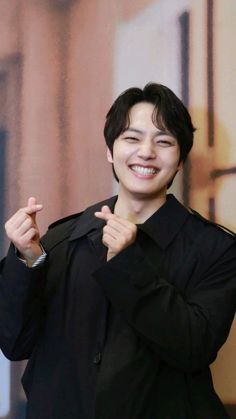 the young man is smiling and pointing to his left side while wearing a black jacket