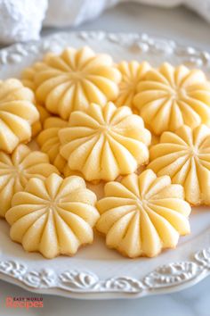 some yellow cookies are on a white plate and one is cut in half to look like flowers