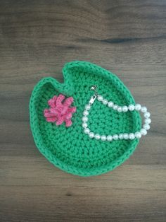 a green crocheted purse with a pink flower on it sitting on top of a wooden table