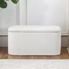 a white storage bench sitting on top of a wooden floor next to a potted plant