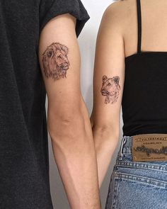 two people holding hands with tattoos on their arms, one has a lion and the other has a dog