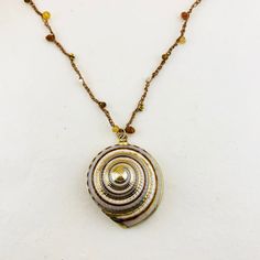 "A sundial seashell trimmed in gold takes center stage, while hessonite garnet, citrine, hematite and mother of pearl dance along hand crocheted silk thread. 14K gold-filled findings finish the look. Seashell measures approximately 1 1/4\" in diameter. Necklace measures 16\" to 19\" in length. Coordinating earrings sold separately." Gold Spiral Jewelry For The Beach, Gold Shell Jewelry With Natural Stones, Gold Bohemian Shell Necklace With Mother Of Pearl, Spiritual Gold Shell Jewelry, Handmade Gold Shell Necklace Spiritual, Luxury Handmade Shell Pendant Necklace, Spiritual Handmade Gold Shell Necklace, Handmade Gold Spiritual Shell Necklace, Handmade Gold Round Shell