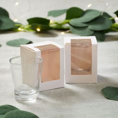 an empty glass next to a white box on a table with greenery around it