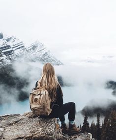 a woman sitting on top of a mountain looking at the mountains