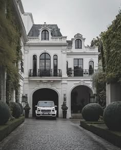 a white truck is parked in front of a large house with trees and bushes around it