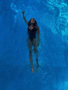 a woman is swimming in the pool with her hand up