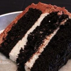 a slice of chocolate cake with white frosting on a silver plate and black background