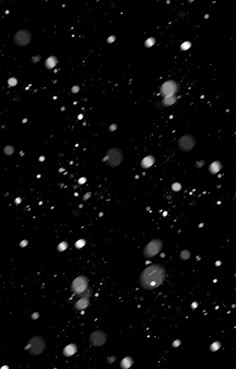 black and white photograph of snow flakes on the night sky with no one in sight