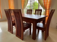 a dining room table and chairs in front of a window with orange drapes on the windowsill