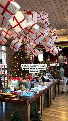 a christmas tree with presents hanging from it's ceiling and people looking at them