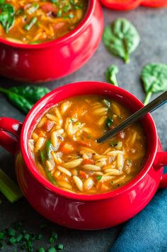 two red bowls filled with pasta soup and garnished with fresh basil on the side