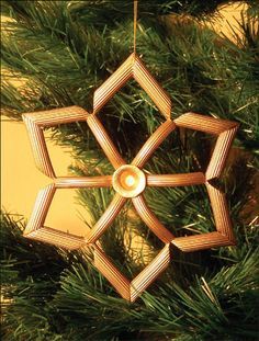 an ornament made out of wood sticks hanging from a christmas tree with pine needles