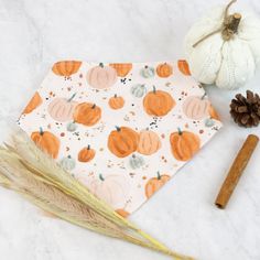 an orange and white napkin with pumpkins on it next to a pine cone, some feathers