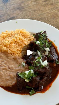 a white plate topped with meat and rice covered in gravy on top of a wooden table