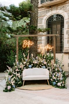 a white couch sitting under a neon sign next to a lush green forest filled with flowers