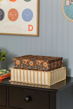 two boxes sitting on top of a wooden table next to a clock and vase with flowers