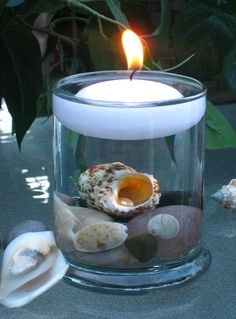 a candle that is inside of a glass bowl filled with rocks and seashells