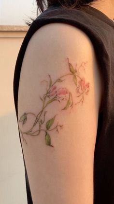 a woman's arm with pink flowers on it and green leaves around the arm