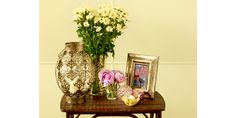 a table with vases and flowers on it next to a framed photo in front of a wall