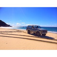 a truck is parked on the beach by the water's edge with tracks in front of it