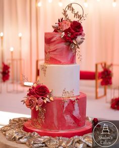 a three tiered wedding cake with red flowers on the top and gold trimmings