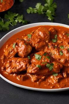 a white bowl filled with meatballs covered in sauce and garnished with cilantro