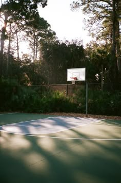 an outdoor basketball court with a basket in the middle and trees behind it, on a sunny day