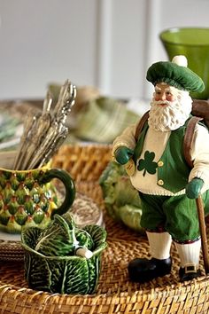 a table topped with plates and cups filled with green decorations on top of a wicker tray