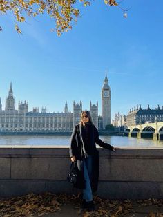 a woman standing on the edge of a wall next to a body of water with big ben in the background