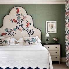 a bedroom with green walls, white bedding and floral embroidered headboard on the wall