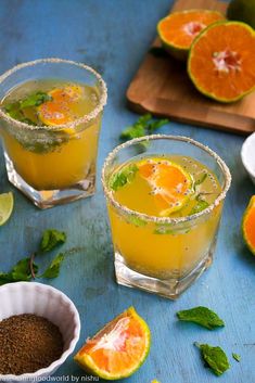 two glasses filled with orange juice and garnished with mint on a blue surface