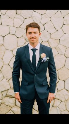 a man wearing a suit and tie standing in front of a stone wall