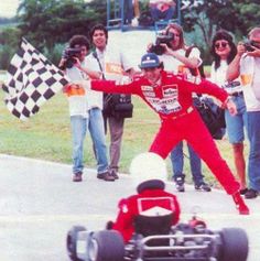 a man in red racing suit standing next to a race car with people behind him