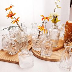 there are many glass vases on the wooden tray and one has flowers in it