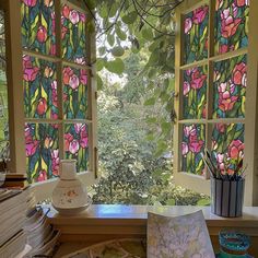 an open window with stained glass flowers on the windowsill and books in front of it